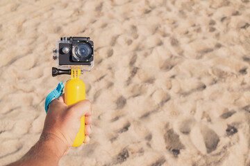 Action camera in the guy's hand close-up. Against the backdrop of a sandy beach.