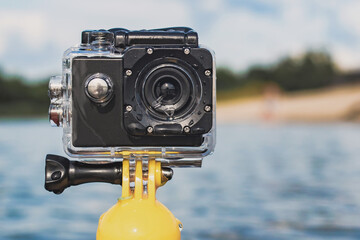 Close-up of an action camera in a waterproof case. Against the background of the water, the shore...