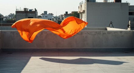 Flowing orange fabric suspended mid-air above urban rooftop with shadow