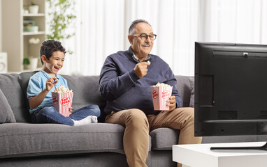 Mature man and a kid watching tv and eating popcorn
