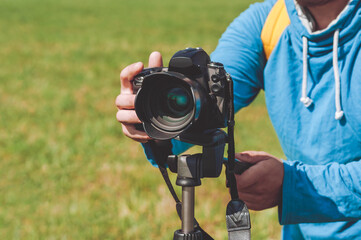 Close-up man with a professional camera shoots from a tripod. Green grass background.