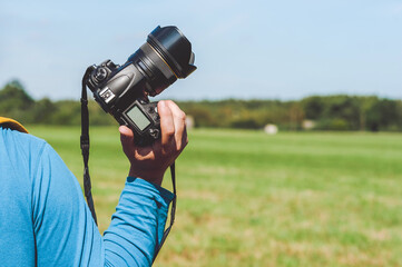Close-up of a professional camera in the hands of a man. Background of green field and blue sky.