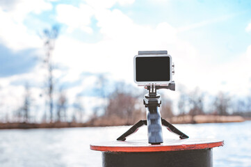Close-up, an action camera on a tripod stands on a pier on a river or lake. Sky background with...