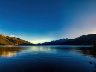 Tranquil Sunset Over Serene Lake with Majestic Mountains and Clear Blue Sky Reflecting on Calm Water Surface at Dusk