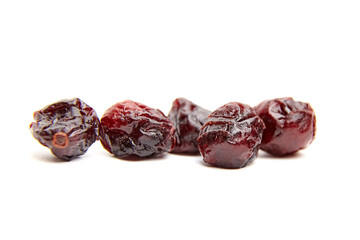 Five dried cranberries arranged in a row on a white surface, showcasing their rich burgundy color, wrinkled texture, and glossy finish in sharp detail