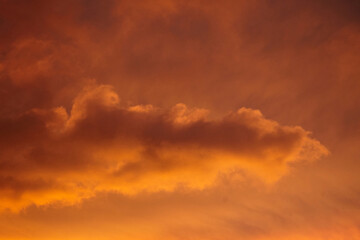 Obraz premium Glowing orange and golden hues color the sky at sunset with soft, wispy clouds drifting gently across the vibrant, illuminated background