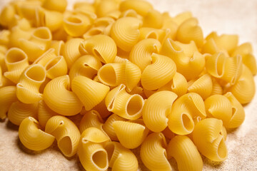 Close-up of uncooked pipe rigate pasta with ribbed, hollow shapes scattered on a light neutral surface, ideal for food packaging and recipe visuals