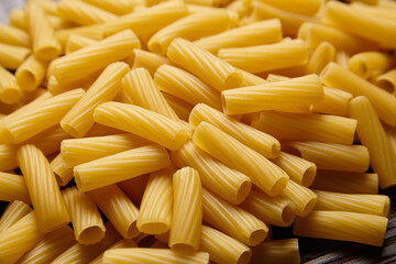 Uncooked tortiglioni pasta in a tight pile, featuring its tubular shape, ridged surface, and golden-yellow color in a detailed close-up.