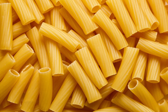 Detailed view of raw tortiglioni pasta showing ridged cylindrical tubes with a golden-yellow hue, ideal for culinary designs or food packaging visuals