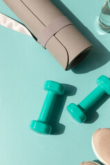Sport or workout concept flat lay with blue dumbbells, sneakers, yoga mat on the blue teal background. Copy space