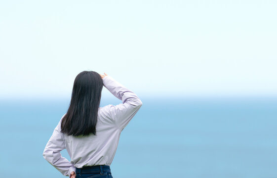 額に手をかざして海を眺める女性