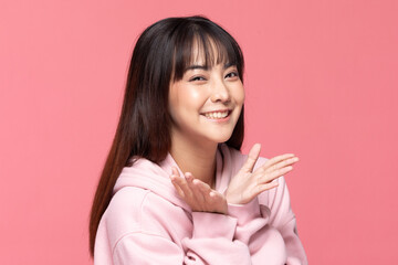 Asian cheerful young woman with long dark hair wearing pink hoodie smiles brightly against pink...