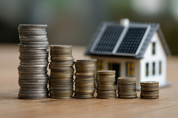 stacks of coins decreasing in height next to a model house with solar panels. Concept of declining home investment, property value, or energy savings. Ideal for finance, mortgage, real estate topics