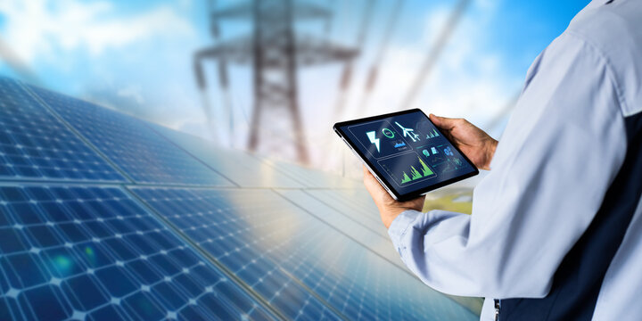 Sustainable energy management system concept.Engineer using digital tablet with solar panels powerplant and high voltage power lines as background