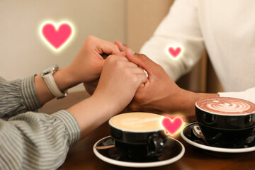 Lovely couple holding hands while drinking coffee in cafe, closeup. Drawn hearts near them
