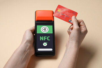 Woman paying with credit card via terminal on dark beige background, closeup