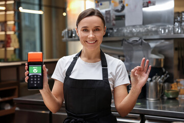 Woman holding payment terminal with NFC system and showing ok in restaurant