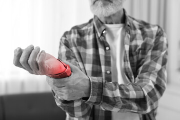 Arthritis. Senior man suffering from wrist pain indoors, closeup. Black and white toning with red...