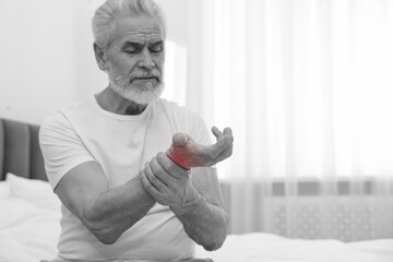 Arthritis. Senior man suffering from wrist pain on bed at home. Black and white toning with red...