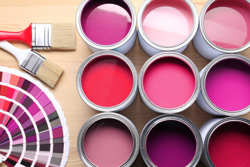 Cans with paint in shades of pink, color palette and brushes on wooden background, top view