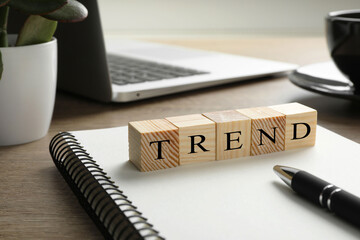 Word Trend made of wooden cubes on notebook. Workplace with stationery and laptop on table