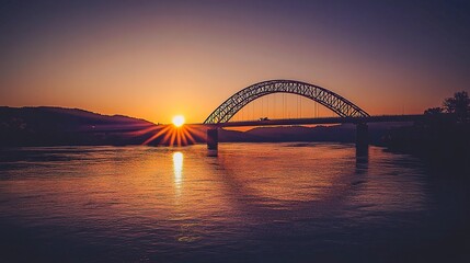 Naklejka premium A breathtaking sunset over the New River Bridge in West Virginia, its iconic steel arch glowing against the clear sky, reflecting in the serene river below. 