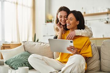 Loving lesbian couple sharing a joyful moment together at home while using a tablet