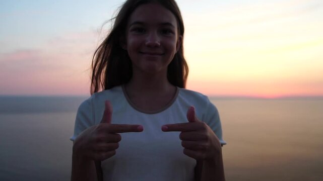 Girl Pointing Sunset Young girl points fingers indicating self over ocean at beautiful sunset