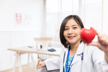 Young woman doctor holding a red heart, at ckinic . Closeup on medical doctor woman showing heart shape gesture