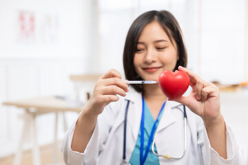 Young woman doctor holding a red heart, at ckinic . Closeup on medical doctor woman showing heart...