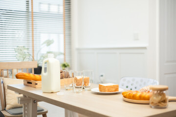 A clean kitchen interior features a table set for a breakfast with orange juice and fruits near a window.