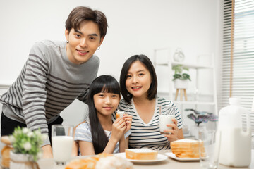 Happy Asian family enjoying breakfast with milk at the kitchen table at home.Parents and daughter enjoying breakfast with milk in a warm, inviting kitchen.