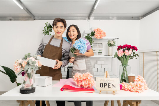 A couple of Asian entrepreneurs using their smartphones to sell flowers online.