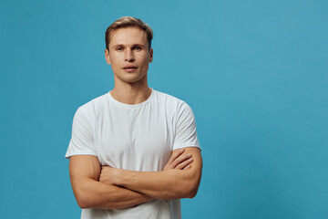 Young serious caucasian man in white t-shirt crossed arms look camera isolated on blue background...