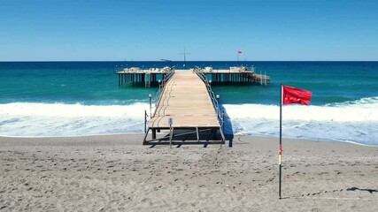 enclosed pier with sun loungers and red flag on beach at resort, slow motion
