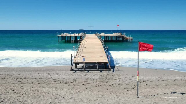 enclosed pier with sun loungers and red flag on beach at resort, slow motion
