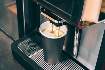Coffee machine pouring espresso into black paper cup, close-up.