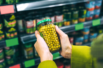 Hands holding jar of green peas in supermarket aisle.