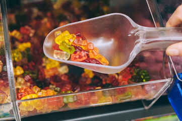 Hand with scoop taking colorful gummy bears in candy store.