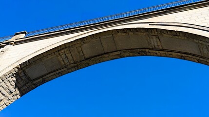 Low-angle view of an arched stone bridge, framed by a cloudless blue sky, symbolizing the blend of tradition and modern civil engineering. Natural tones, wide shot. 