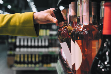 Hand picking rose wine bottle from store shelf.
