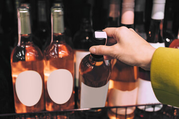 Hand taking white wine bottle with blank label from shelf.