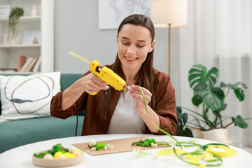 Woman with hot glue gun making craft at table indoors