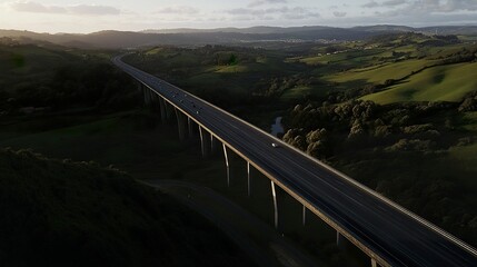 Obraz premium Overhead dusk scene of a motorway bridge connecting towns, spanning a lush valley of hills and forests bathed in gentle twilight tones 