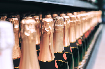 Row of sparkling wine bottles with gold foil on shelf.