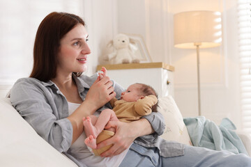 Mother with her cute newborn baby on sofa indoors