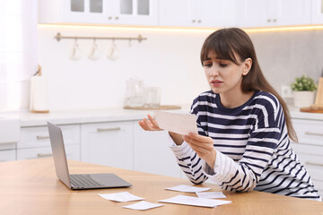 Paying bills. Upset woman with different invoices and laptop at wooden table indoors