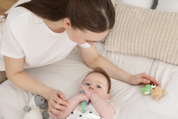 Mother and her cute little baby with rattle on bed at home