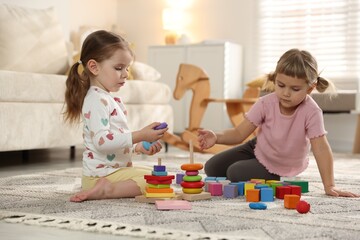Fototapeta premium Cute little sisters playing with toy pyramids on floor at home