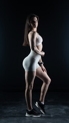 Young beautiful woman with athletic body on dark background. Fitness girl